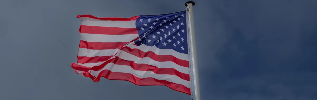 A vibrant American flag waving in the wind against a clear sky at Omaha Beach, France.
