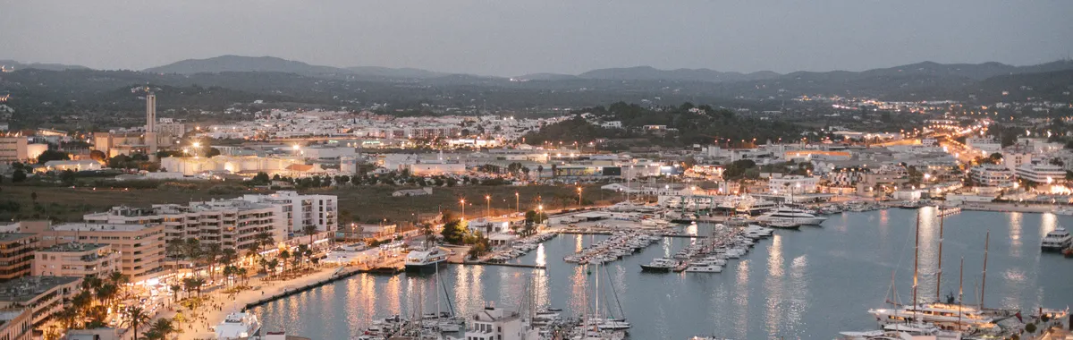 A scenic aerial view of Ibiza's marina at dusk, showcasing vibrant city lights and bustling harbor in Spain.