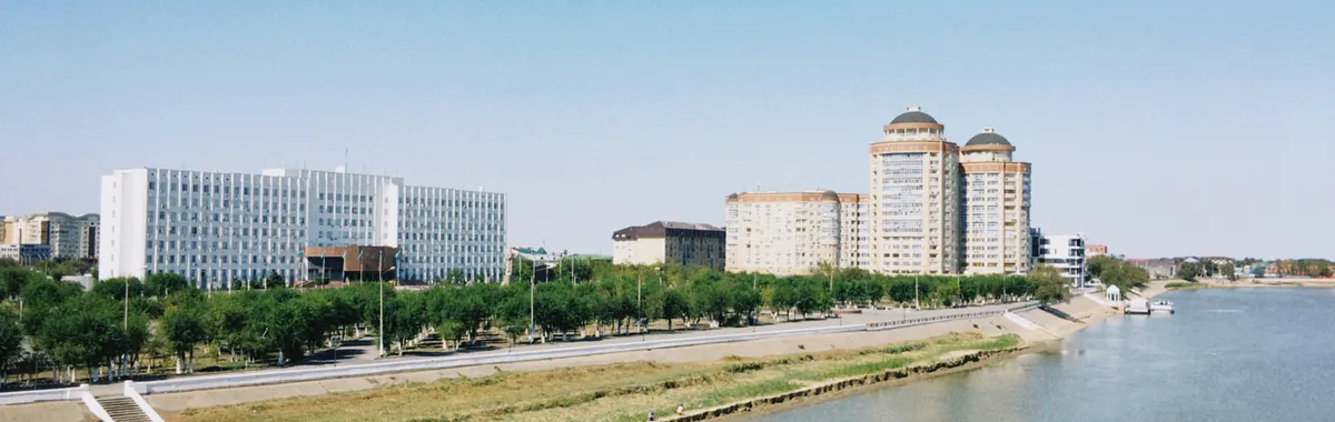 A scenic daytime view of Atyrau city skyline with modern buildings along the Ural River in Kazakhstan.