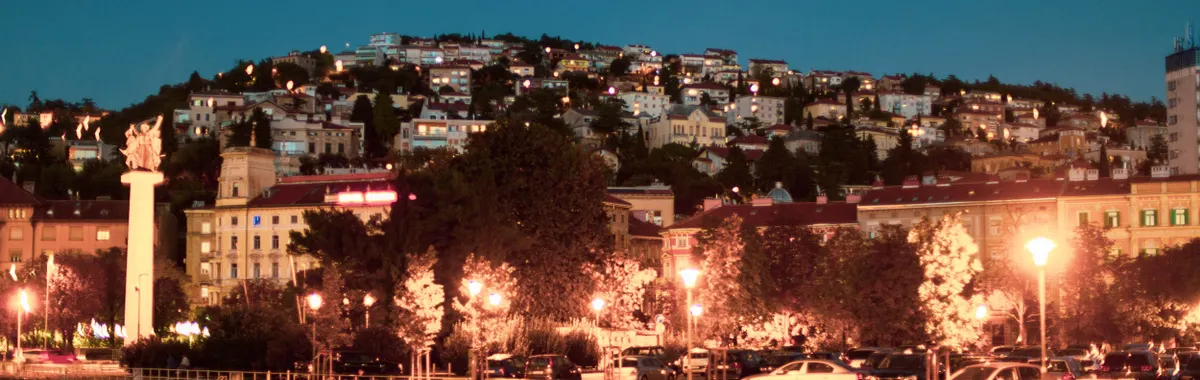 A vibrant night view of the waterfront in Rijeka, Croatia, with boats and city lights.