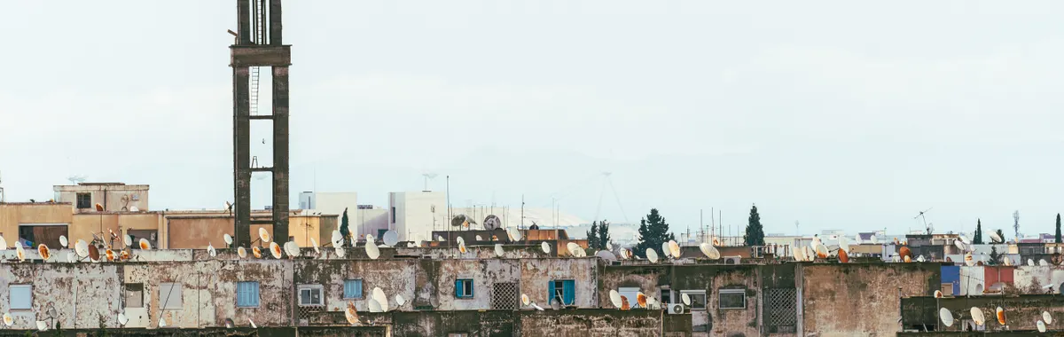 Urban rooftops with satellite dishes beneath a towering minaret in Tunis, Tunisia.