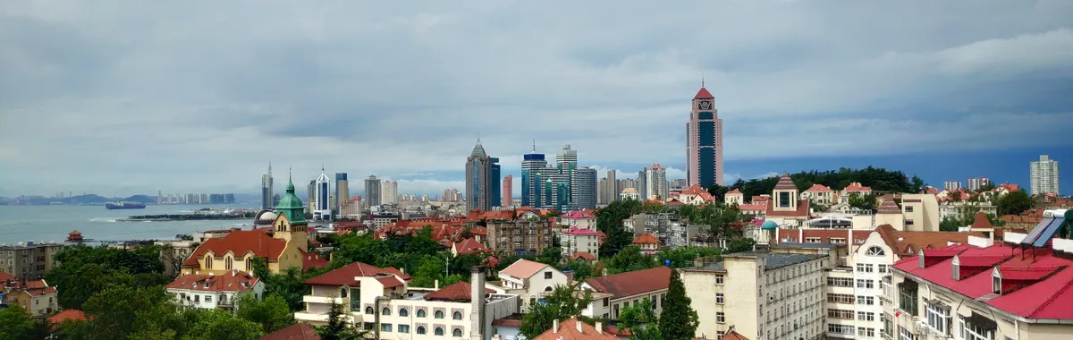 A scenic view of Qingdao's skyline with historical buildings and modern skyscrapers under a cloudy sky.