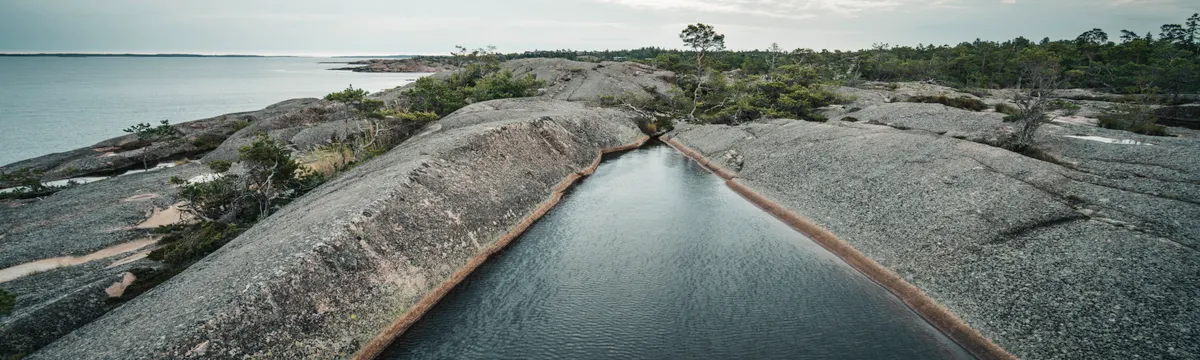 איי אולנד: A tranquil rocky coastline with a natural water pool in the Åland Islands.