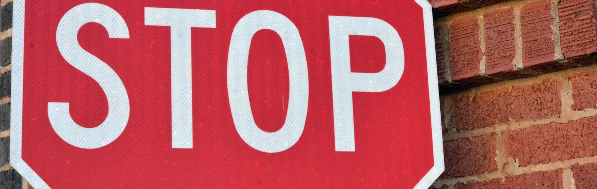 Red stop sign mounted on a brick wall in Henderson, Texas, during the day.