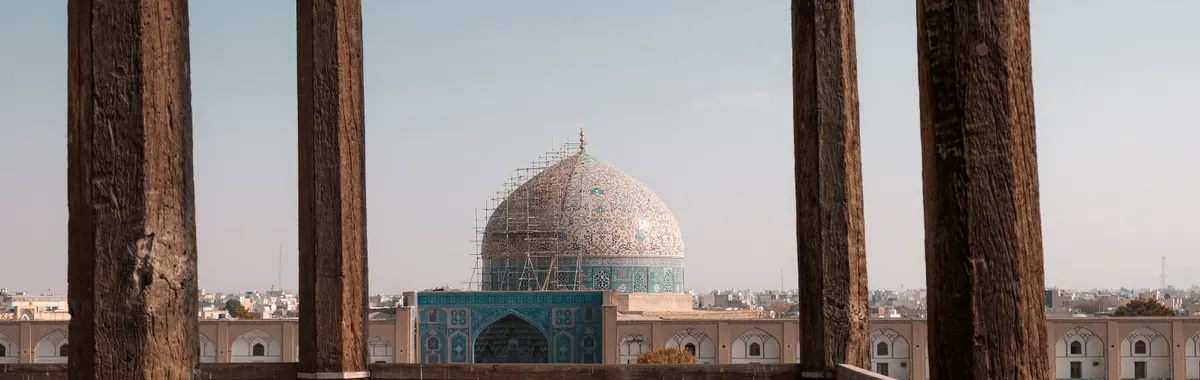 Beautiful capture of the Shah Mosque in Isfahan, featuring intricate architecture behind wooden pillars.