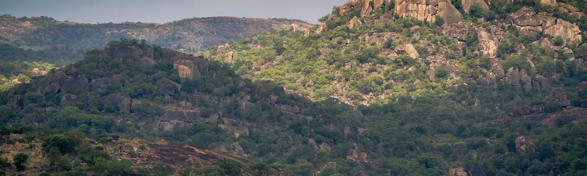 זימבבואה: Aerial view of lush, rocky hills in Zimbabwe under a cloudy sky, showcasing natural beauty.