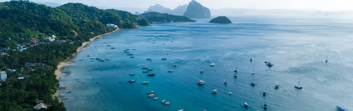Stunning aerial view of El Nido's vibrant blue bay with lush greenery and boats, capturing the essence of the Philippines' natural beauty.