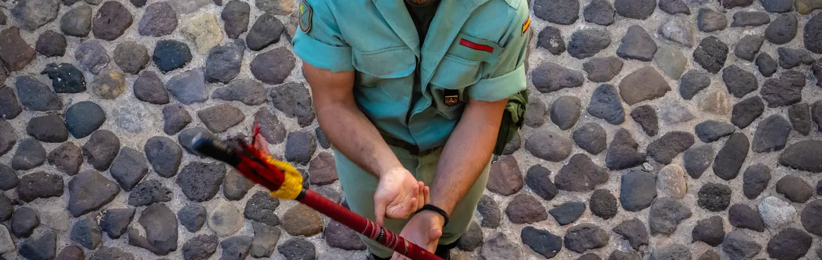 A soldier in uniform kneels on a cobblestone street holding a ceremonial spear in Melilla, Spain.
