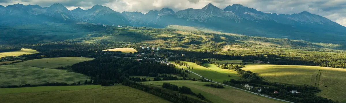 סלובקיה: Stunning aerial view of Vysoké Tatry in Slovakia, showcasing lush fields and dramatic mountain ranges.