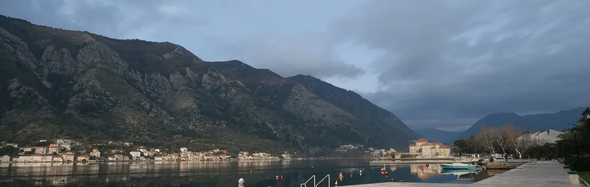Peaceful morning view of Kotor Bay in Montenegro, showcasing calm waters and mountainous backdrop.