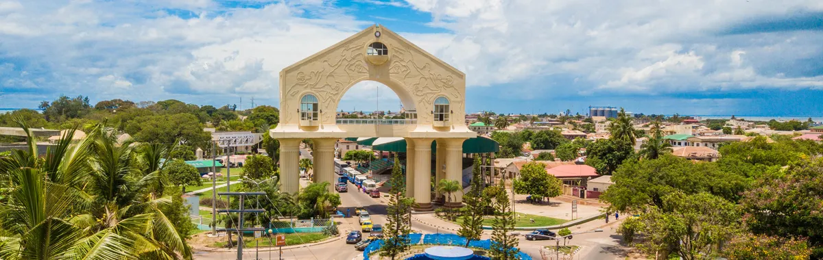Scenic aerial view of Arch 22 in Banjul, The Gambia amid lush greenery and cloudy sky.