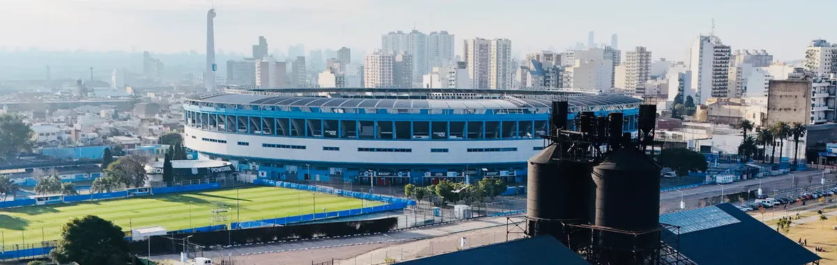 A panoramic aerial view of a stadium in Avellaneda, Buenos Aires with cityscape in the background.