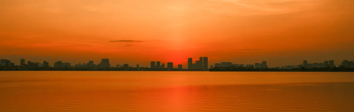 A vivid sunset casts a golden hue over the serene waters of Hanoi, Vietnam.