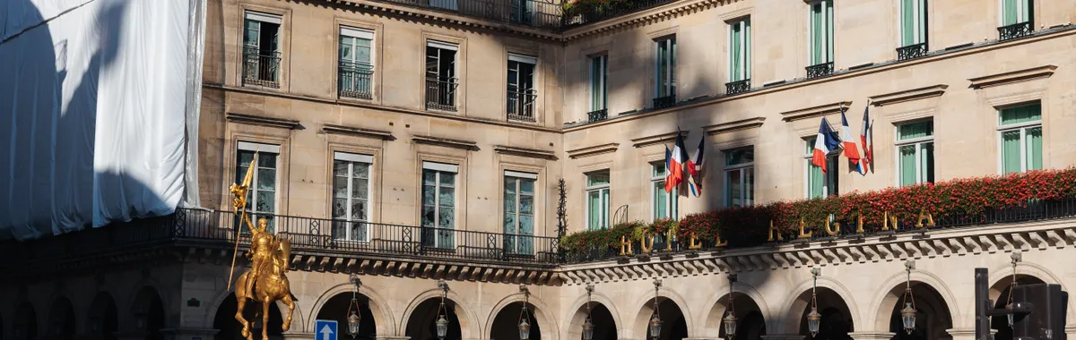 Historic Hotel Regina and Joan of Arc statue in Paris bustling with pedestrians and traffic.