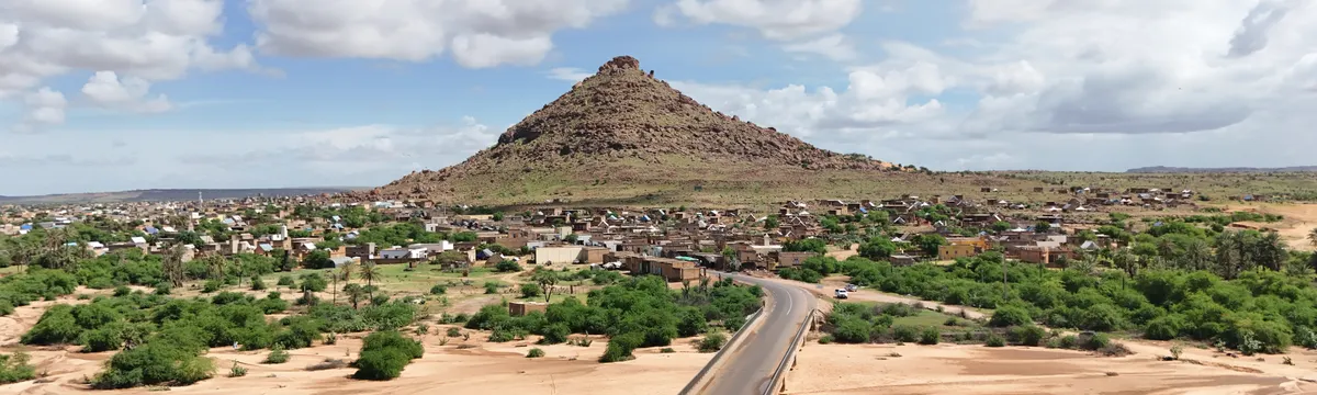 מאלי: Aerial view of Bafoulabe with a prominent rocky hill under a bright, cloudy sky.
