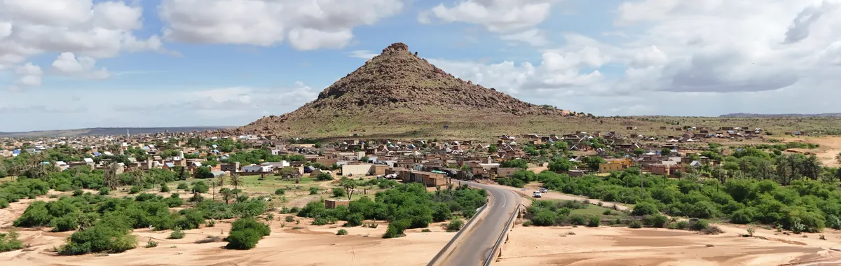 מאלי: Aerial view of Bafoulabe with a prominent rocky hill under a bright, cloudy sky.