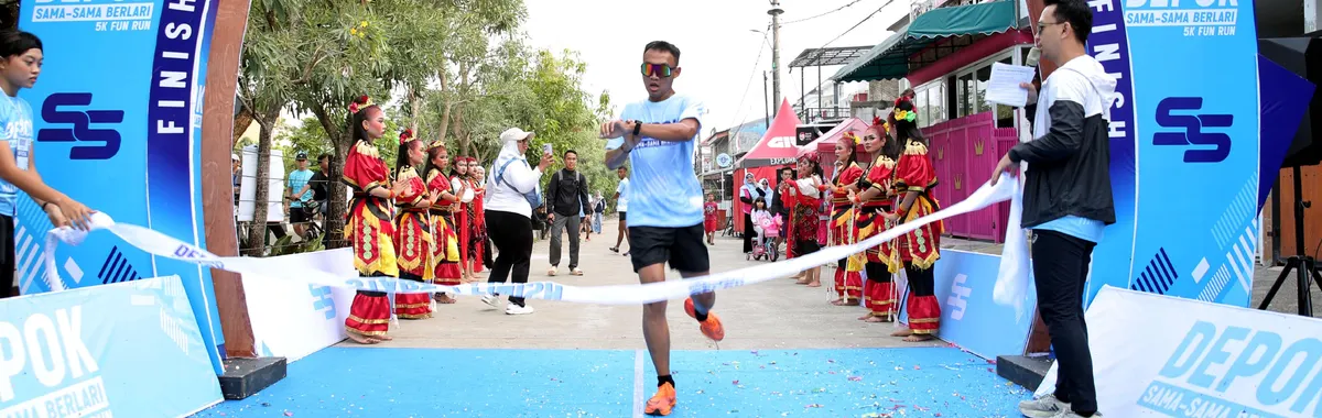 Runner completing Depok 5K Fun Run with spectators in traditional attire. Outdoor event.