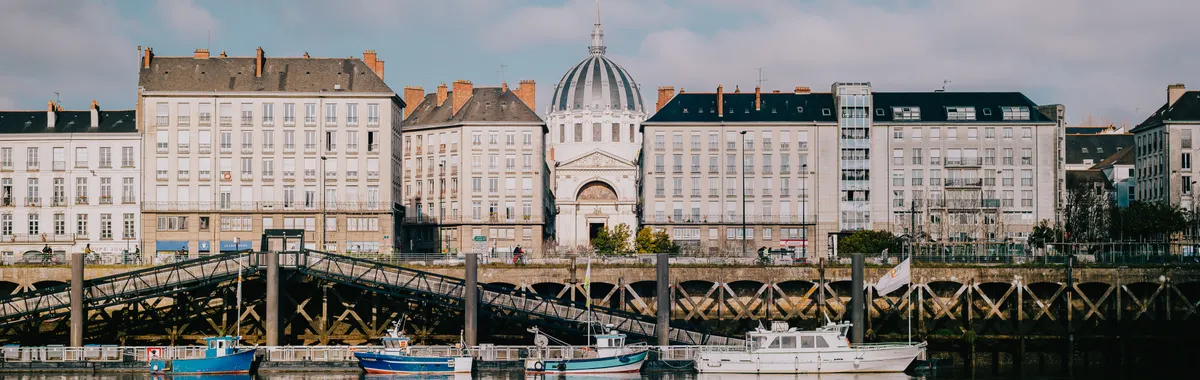 Architecture of Nantes with reflections on the Loire River under a bright sky.
