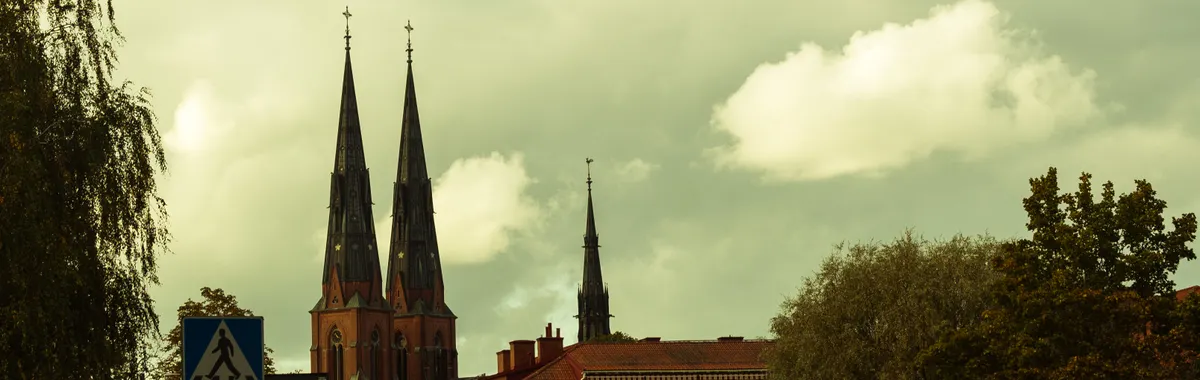 Scenic view of Uppsala Cathedral with autumn foliage under cloudy skies.