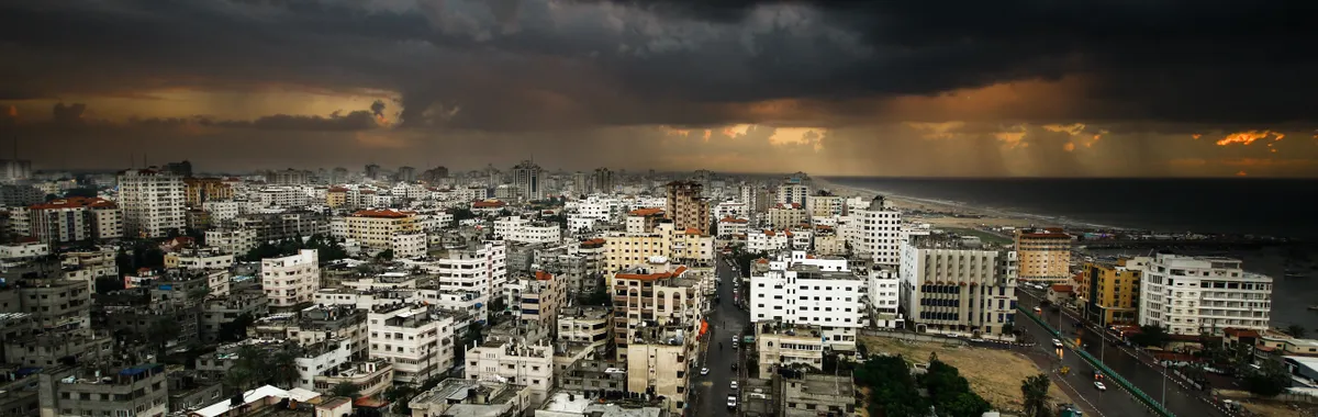 Moody city view of Gaza under dark clouds with rain on the horizon.