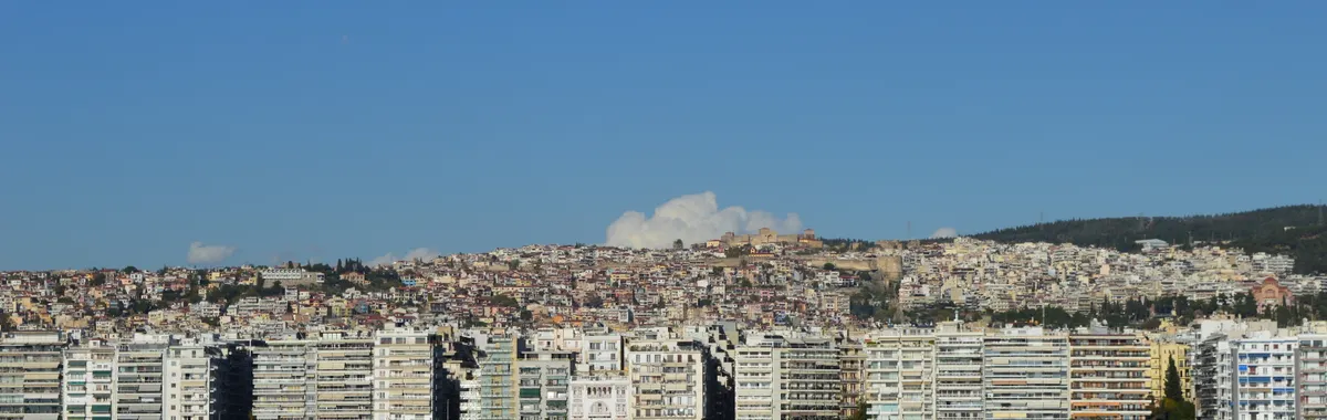 Panoramic view of Thessaloniki's waterfront skyline with residential buildings and blue sky.