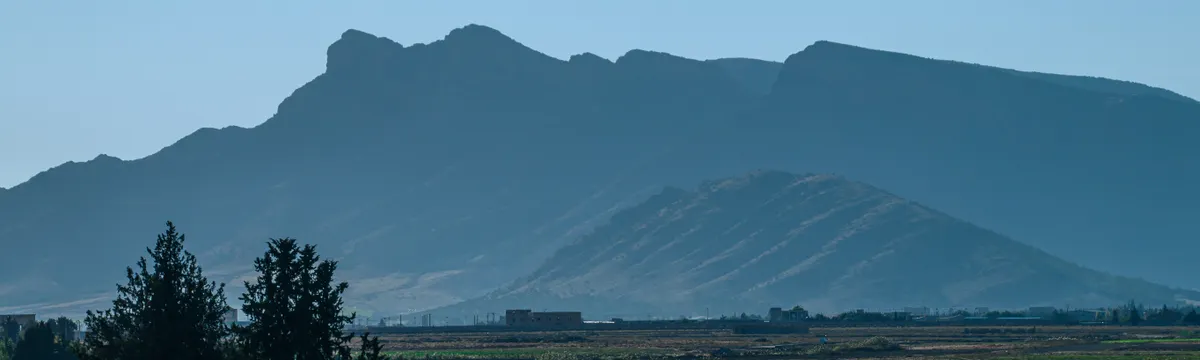 אלג׳יריה: Breathtaking view of verdant fields and mountainous backdrop in Aïn M'lila, Algeria captured under a bright blue sky.