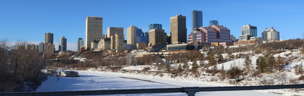 A scenic view of Edmonton's skyline during winter with a snow-covered river in the foreground.