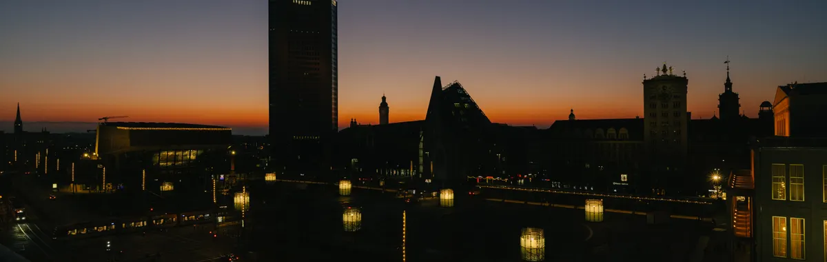 Dusk view of Leipzig's skyline with city lights and orange twilight sky.