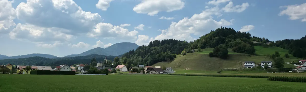 סלובניה: Peaceful rural landscape with rolling hills and small village under a blue sky in Slovenia.