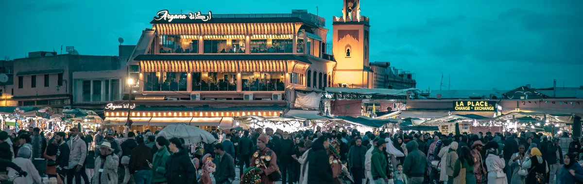 Crowd gathered at iconic Jemaa el-Fnaa square in Marrakesh during dusk, vibrant and lively atmosphere.