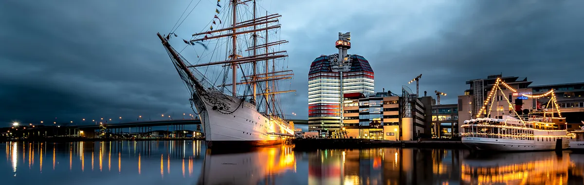 Twilight view of Gothenburg's waterfront featuring Lilla Bommen and sailing ships.