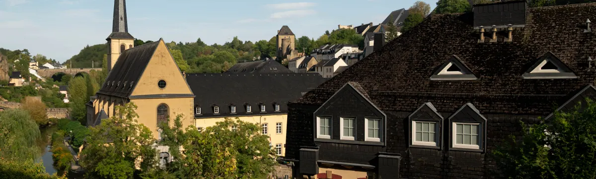 לוקסמבורג: A picturesque view of Luxembourg City featuring historic architecture and lush greenery under a clear blue sky.