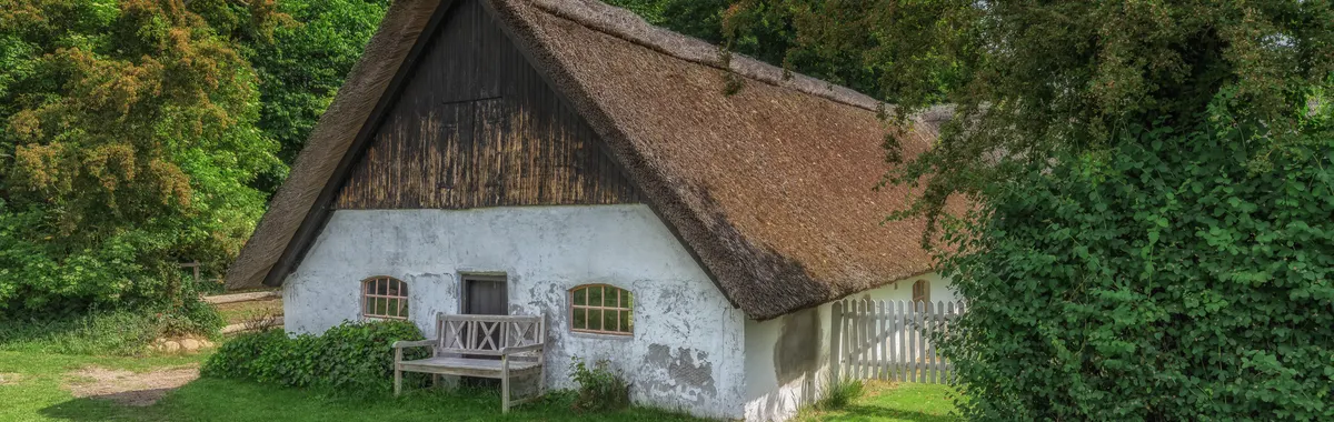 Idyllic thatched cottage surrounded by lush greenery in Århus, Denmark.