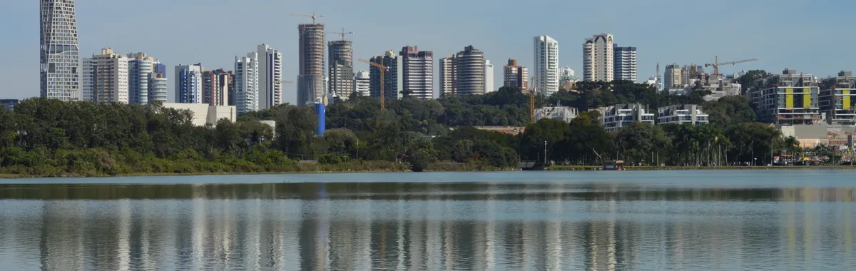 Skyline of Curitiba, Brazil, reflecting on a serene lake under a clear blue sky.