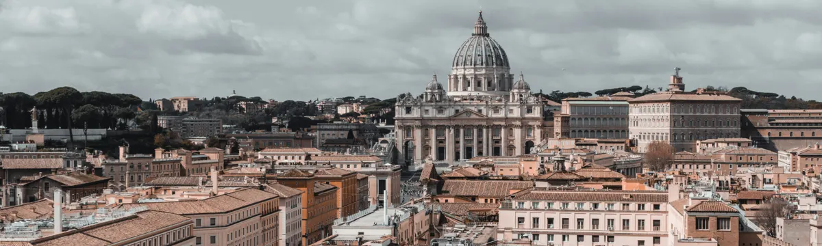 הוותיקן: Skyline view of Vatican City featuring St. Peter's Basilica under a cloudy sky.