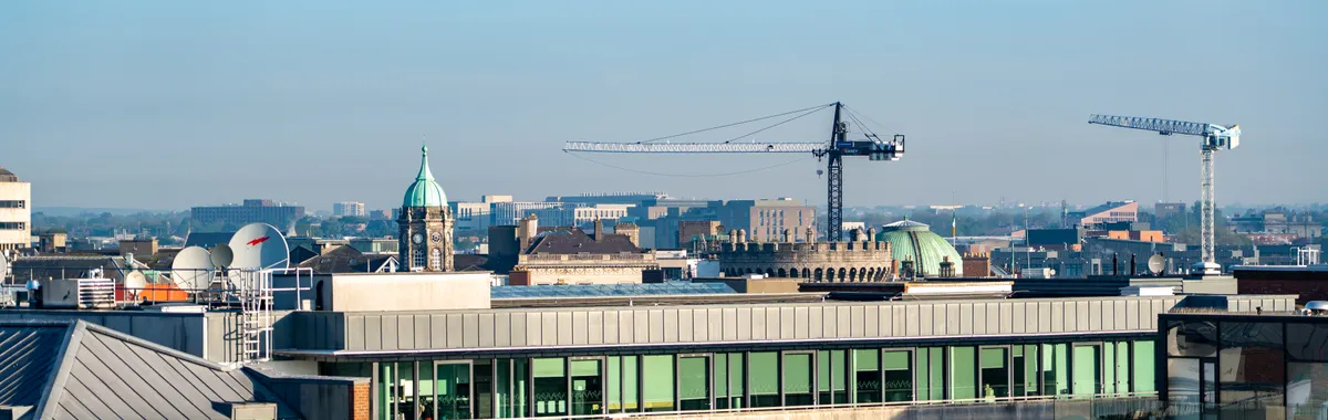 A vibrant view of Dublin's cityscape featuring construction cranes and iconic architecture under a clear blue sky.