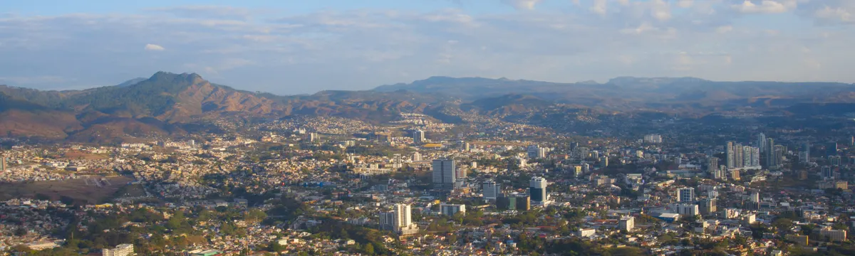 הונדורס: Aerial view of Tegucigalpa city with mountain backdrop under a clear blue sky.