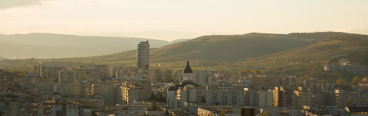 A scenic view of Cluj-Napoca city against the backdrop of rolling hills at sunset.