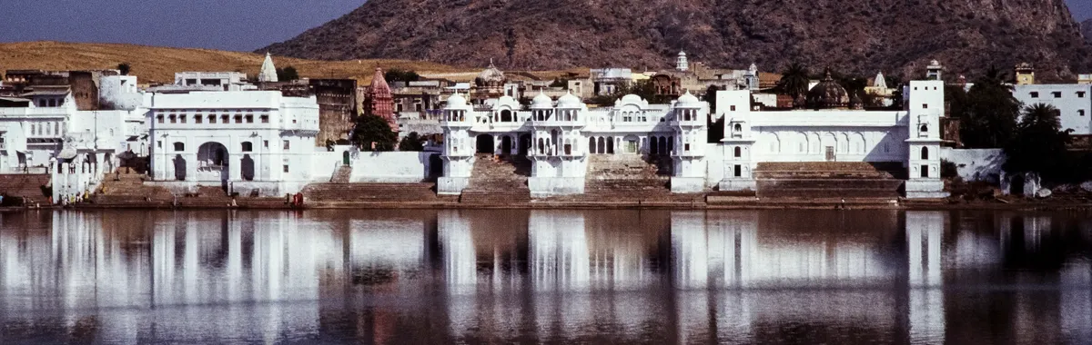 Reflective view of Pushkar Lake with surrounding architecture and hills in India.
