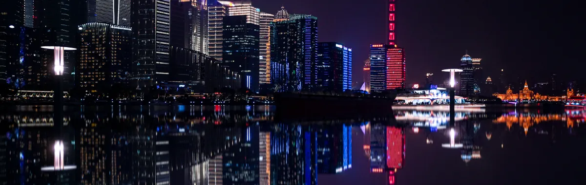 Dazzling night view of Shanghai's Pudong skyline with the iconic Oriental Pearl Tower reflecting on the water.