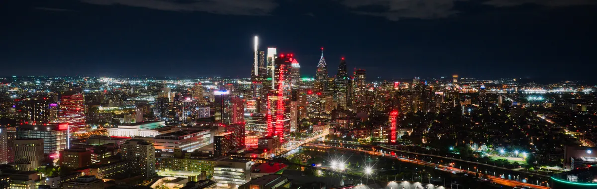 A breathtaking aerial view of Philadelphia's illuminated skyline at night, highlighting the vibrant cityscape and a prominent stadium.