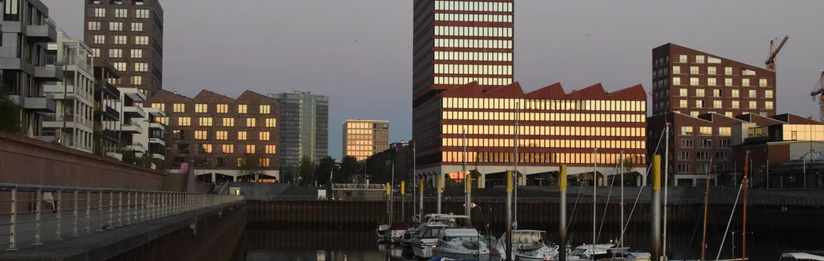 Skyline of modern buildings reflecting in the water at sunset, with boats in Bremen's harbor.