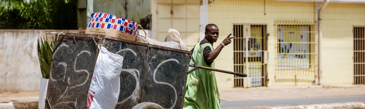 טוגו: A street vendor in a green dress pushes a cart along an urban street in Lomé, Togo.