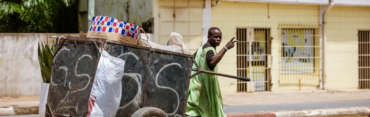 טוגו: A street vendor in a green dress pushes a cart along an urban street in Lomé, Togo.