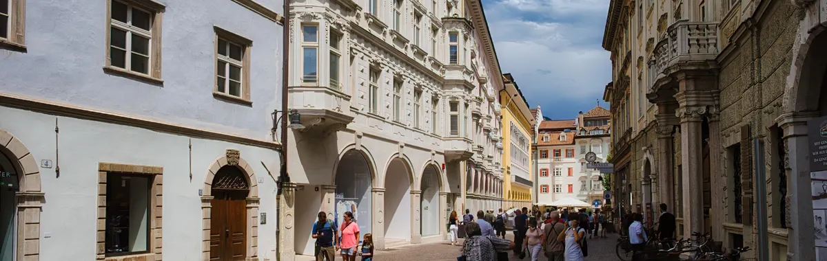 A bustling cobblestone street in Bolzano, Italy, with historic architecture and casual pedestrians.