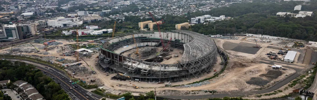 Aerial view of a large stadium under construction in Tegucigalpa, Honduras, surrounded by cityscape and greenery.