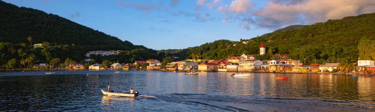 גוואדלופ: A picturesque sunset over Deshaies Bay, Guadeloupe, with a small boat in the foreground.