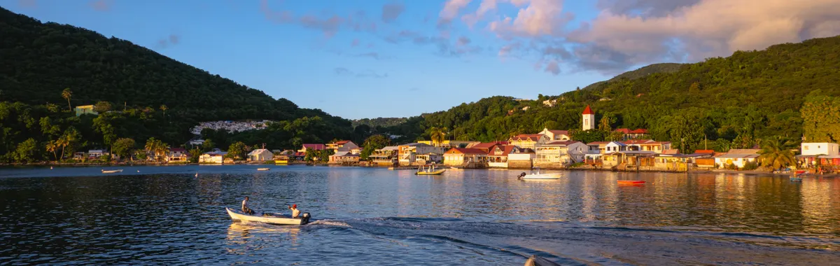 גוואדלופ: A picturesque sunset over Deshaies Bay, Guadeloupe, with a small boat in the foreground.