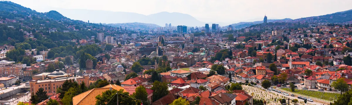 בוסניה והרצגובינה: Aerial view of Sarajevo, showcasing cityscape, red rooftops, and distant mountains.