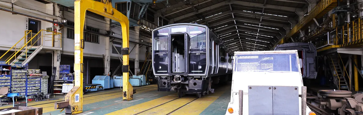 Interior view of a train maintenance facility in Kitakyushu, Japan showing trains and equipment.